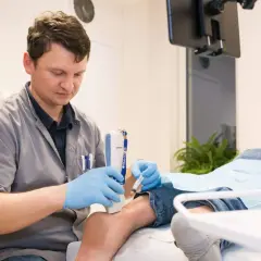 Lekarz podaje pacjentowi osocze bogatopłytkowe za pomocą strzykawki, używając aparatu USG do precyzyjnego nakłucia.