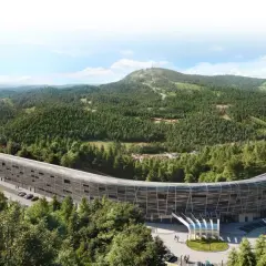 Nowoczesny, zakrzywiony budynek hotelu Mercure Szczyrk Resort otoczony lasem i górami.