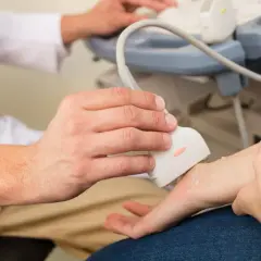 Lekarz wykonuje usg nadgarstka pacjenta, używając sondy aparatu do ultrasonografii.