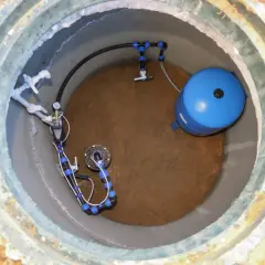 Wykończenie studni głębinowej: niebieski zbiornik hydroforowy i system rur z manometrem.