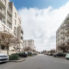 Nowoczesne bloki mieszkalne na osiedlu Zielona Italia, z balkonami i parkingiem pełnym samochodów.
