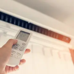 Mano sujetando control remoto de aire acondicionado para combatir el calor. La pantalla muestra 22 grados.