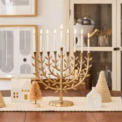 A golden menorah with lit candles is the centerpiece of this Chanukah decorating idea, surrounded by miniature houses and trees.