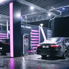 Nowoczesna bezdotykowa myjnia samochodowa Pink Wash nocą. Czarne samochody pokryte pianą, lśniące od wody podłogi i neonowe światła tworzą futurystyczny klimat.