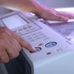 Dłoń naciska przycisk na panelu drukarki, druga dłoń przytrzymuje papier na skanerze.