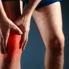 Mężczyzna trzyma się za zaczerwienione kolano, odczuwając nieprzyjemne szczypanie w kolanie.