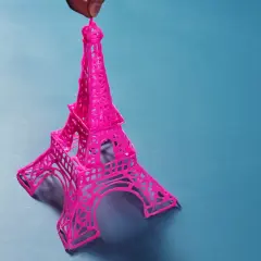 Una manualidad de la Torre Eiffel rosa, creada con filamento, sostenida por un dedo.