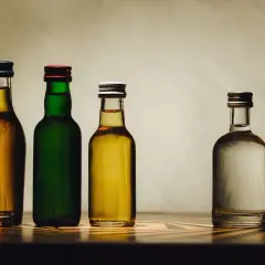 Cztery butelki z płynami: dwie z bursztynowym alkoholem, jedna z zielonym płynem i jedna z przezroczystym. Może to być domowy samogon.