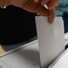 Hand wirft Stimmzettel in Wahlurne.