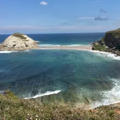 Vista de la Virgen del Mar en Santander, con una isla rocosa y aguas turquesas.