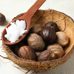 Noci di karité in una ciotola di cocco, con un cucchiaio di burro bianco. Il burro di karité serve per nutrire e idratare la pelle.