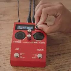 Dłoń kręci gałką na czerwonym looperze do gitary Boss RC-10R, ustawiając rytm funk.