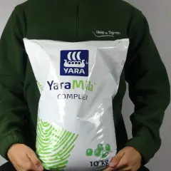 Osoba w zielonej bluzie trzyma worek nawozu YaraMila Complex o wadze 10 kg.
