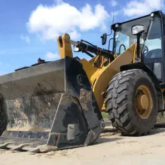Żółta koparko-ładowarka z dużym czerdakiem na tle błękitnego nieba z chmurami. Zastanawiasz się, ile pali koparko ładowarka na godzinę?