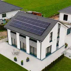 Nowoczesny biały dom z panelami słonecznymi na dachu, tarasem i ogrodem.