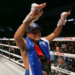 A victorious boxer, representing Nicaraguan pride, raises his taped hands in triumph in a packed arena.