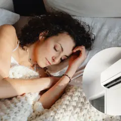 Mujer durmiendo plácidamente bajo una manta, con el aire acondicionado a 22 grados creando un ambiente perfecto para el descanso.
