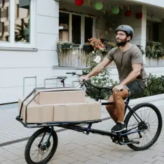 Mann liefert Pakete mit einem Lastenrad. Eine gute Lastenrad Versicherung schützt vor unerwarteten Schäden.