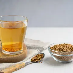 Glas mit Bockshornklee-Tee und Samen daneben. Informieren Sie sich über mögliche bockshornklee nebenwirkungen, bevor Sie ihn konsumieren.