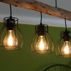 Lámpara de techo con tres bombillas Edison dentro de jaulas metálicas, colgadas de una rama de madera rústica.