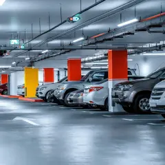 Jasne, oto opis alternatywny:

Rząd samochodów zaparkowanych pod jasnym oświetleniem parkingu. Kolorowe słupy i strzałki kierunkowe wskazują drogę.