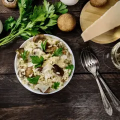 Risotto ai funghi cremoso, guarnito con prezzemolo fresco e scaglie di parmigiano. Un bicchiere di vino bianco completa questo perfetto abbinamento vino funghi.