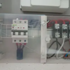 Trzybiegunowy wyłącznik nadprądowy w obudowie z przezroczystego plastiku, podłączony do przewodów.