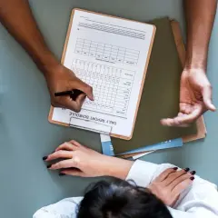 La segretaria studio compila un report giornaliero. Mani che lavorano su documenti, un bicchiere d'acqua.