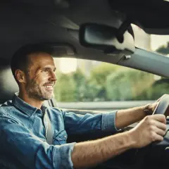 Uśmiechnięty mężczyzna za kierownicą, dbający o ochronę zniżek OC. Bezpieczna jazda to podstawa.
