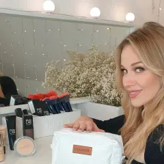 Blondynka z kosmetykami, szuka inspiracji, czym pomalować twarz na biało.
