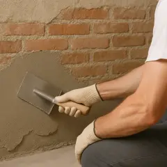 Man con guantes aplica revoque a pared de ladrillos, un paso clave para saber como quitar la humedad para siempre.