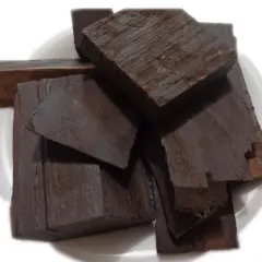 Pezzi di legno scuro, forse ebano, il legno più costoso del mondo, su un piatto bianco.