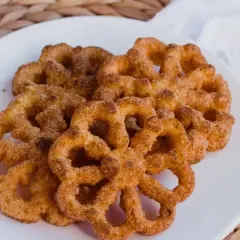 Un plato blanco con varios buñuelos de viento espolvoreados con canela y azúcar.