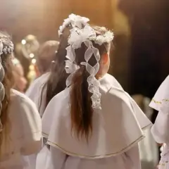 Dzieci w białych strojach, z wiankami na głowach, czekają na moment, kiedy jest komunia.