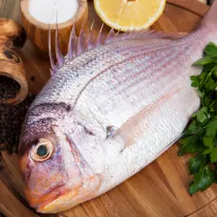 Un pescado rojo, listo para cocinar con perejil, limón, sal y pimienta negra.