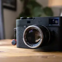 A black Leica M10P camera with a Carl Zeiss Sonnar lens sits on a wooden table, ready to capture life's moments.