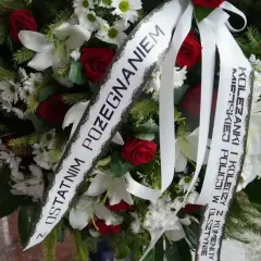 Wieniec z białych lilii, czerwonych róż i zieleni. Na białej szarfie widnieje oryginalny napis na szarfie pogrzebowej: "Z ostatnim pożegnaniem Koleżanki i Koledzy z Komendy Policji w Olsztynie".