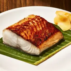 A perfectly seared Nobu miso black cod recipe, served on a banana leaf with pickled ginger.