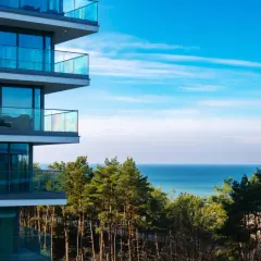 Nowoczesny budynek z balkonami i widokiem na morze. W oddali las i błękitne niebo. Idealne miejsce na wypoczynek w Wave Międzyzdroje Resort&SPA.