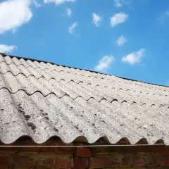 Stary dach pokryty eternitem, materiałem zawierającym azbest, pod błękitnym niebem z chmurami.