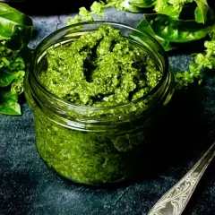 Frisches Basilikum-Pesto in einem Glas, bereit für ein köstliches basilikum pesto rezept. Daneben ein Löffel und grüne Basilikumblätter.