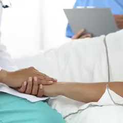 Lekarz uspokaja pacjenta, który leży w łóżku. W tle inny medyk notuje coś na kartce. Ustawa o niepełnosprawnych bez kolejki zapewnia im priorytet.