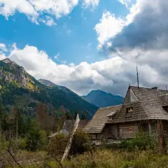 Drewniane chaty w górach jesienią, otoczone lasem i skalistymi szczytami.