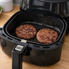 Due hamburger succulenti cuociono nella friggitrice ad aria, pronti per essere serviti con pane tostato e insalata.