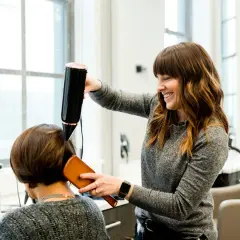 Estilista sonríe mientras seca el cabello de una clienta. Un buen momento para cortarse el pelo es cuando te sientes renovada.
