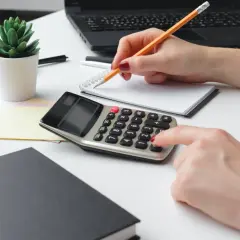 Kobieta liczy podatek od dywidendy, jaki PIT. Na biurku kalkulator, notatnik i laptop.