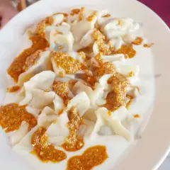 En tallrik med manti, små dumplings i en krämig sås med en kryddig topping. Perfekt för ett manti recept.