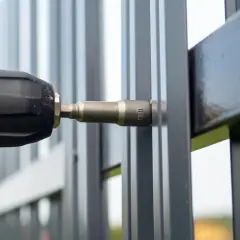 Montaż elektrozaczepu do furtki. Wiertarka z nasadką 8mm przykręca element do metalowej konstrukcji.