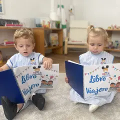 Niños leyendo un libro viajero infantil, con dibujos de cohetes y globos aerostáticos.