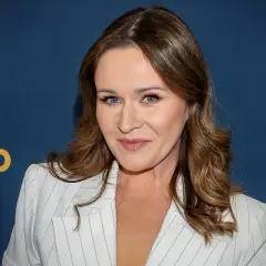Ewa Błachnio, znana z kabaretów, w białej marynarce w prążki, uśmiecha się do obiektywu.